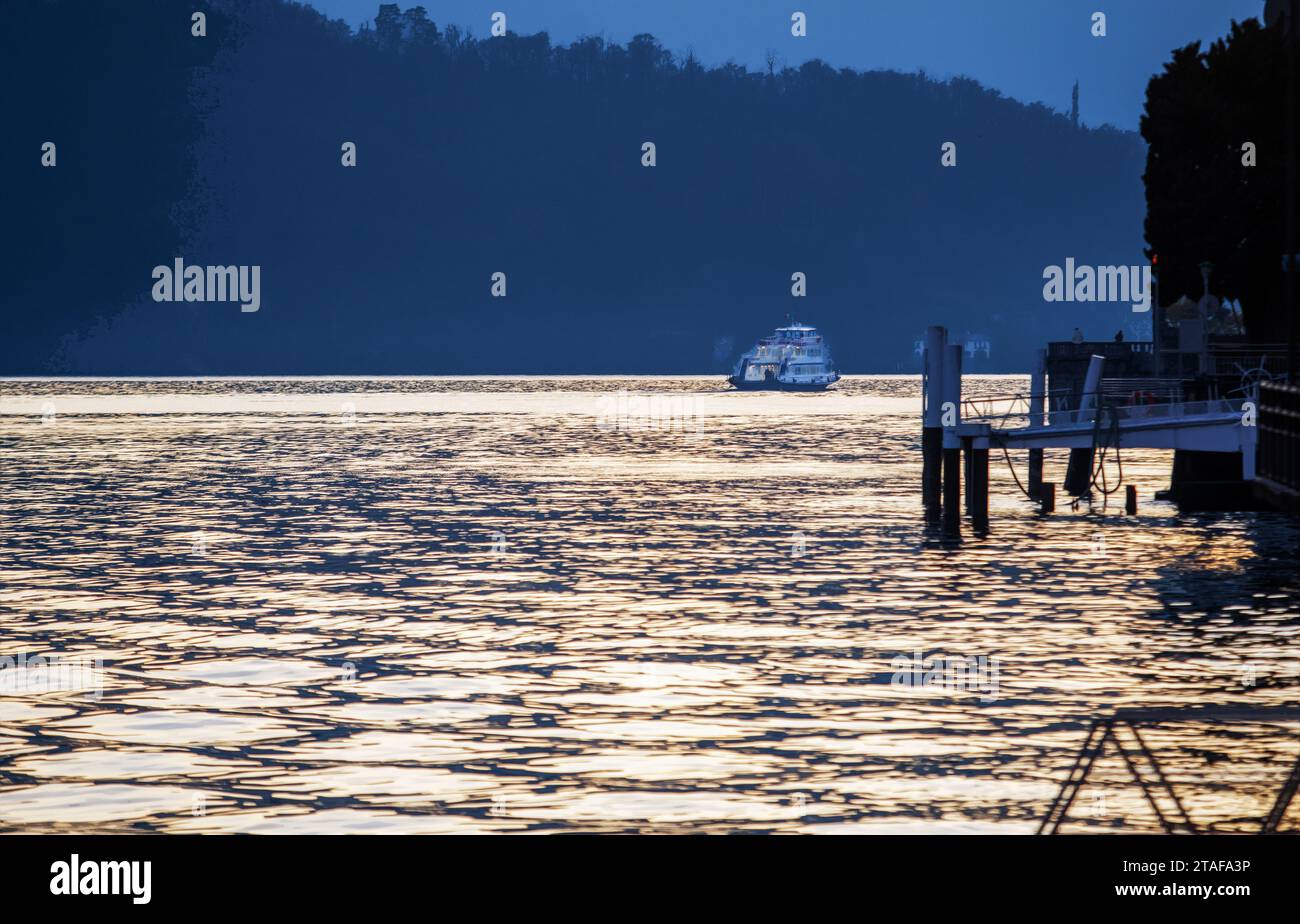 Una piccola nave trasporta le persone dai villaggi alla città di Como, a sud del lago di Como, un cielo argentato al tramonto. Breve viaggio durante la settimana di Natale. Foto Stock