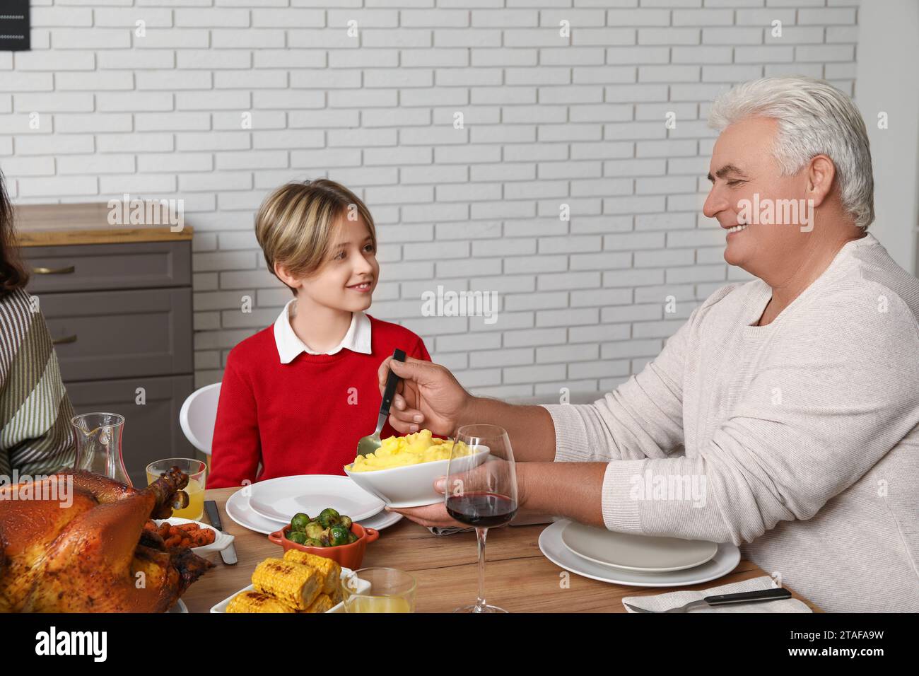 Un uomo maturo che mette da mangiare sul piatto del suo piccolo nipote al tavolo delle feste per il giorno del Ringraziamento Foto Stock