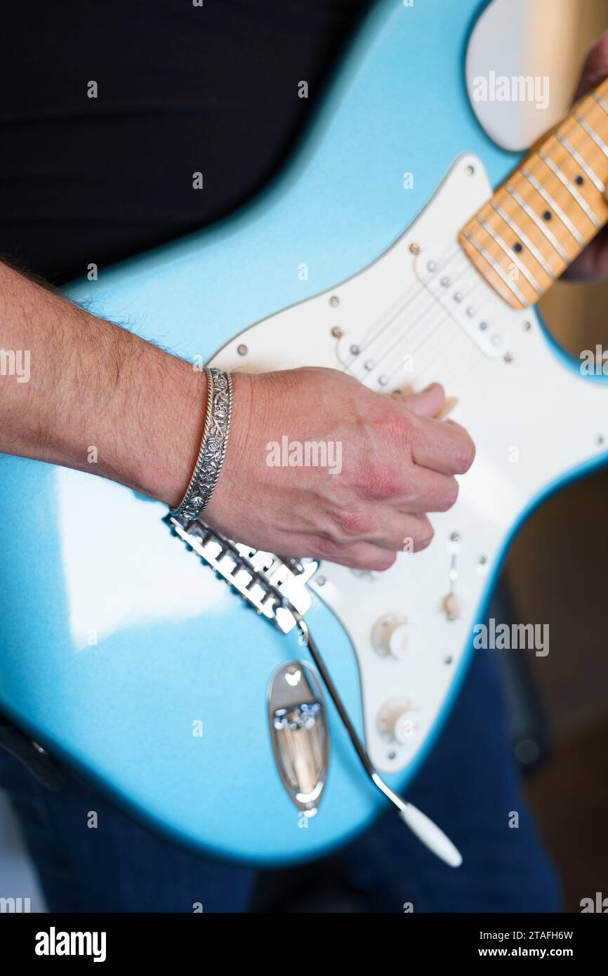 Primo piano di un musicista rock che suona una chitarra elettrica blu e indossa un bracciale con polsino d'argento Foto Stock