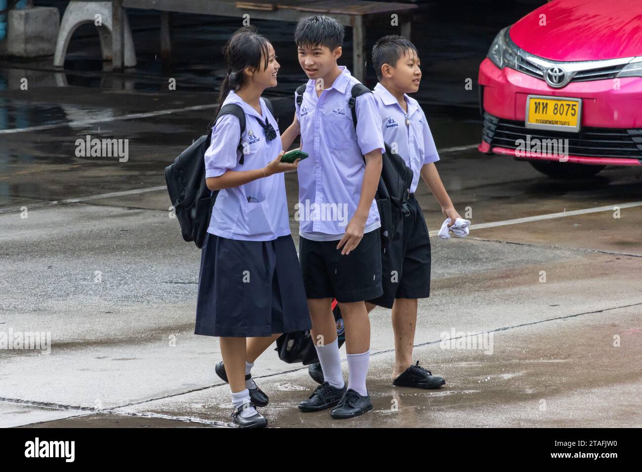 SAMUT PRAKAN, THAILANDIA, 20 settembre 2023, allegri scolari in uniforme camminano lungo una strada piovosa Foto Stock