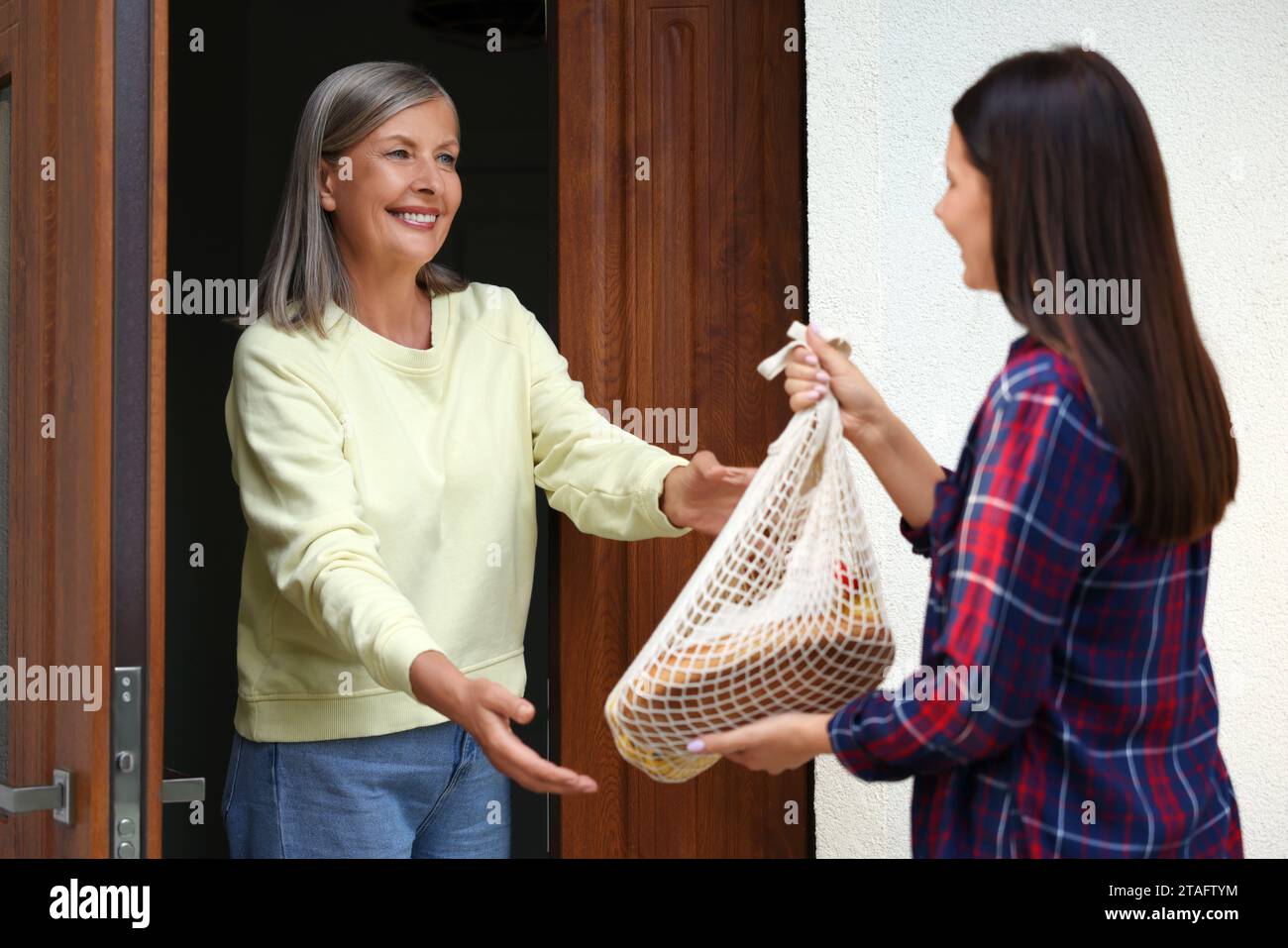 Giovane donna con un sacco di prodotti che aiuta il suo vicino più anziano all'aperto Foto Stock