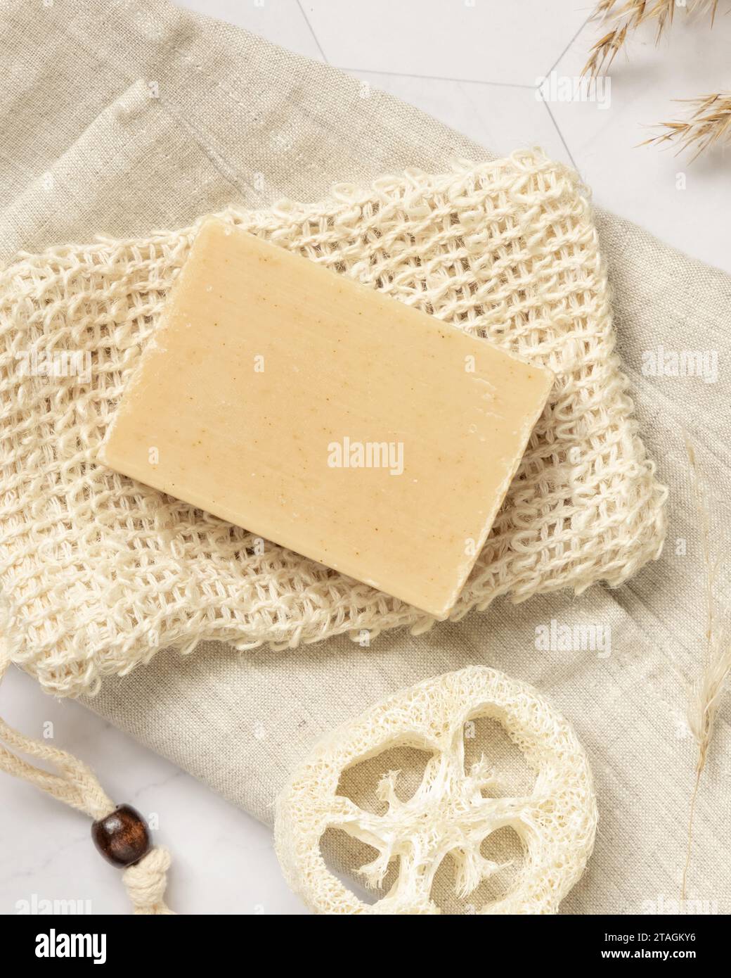 Sapone beige su sacchetto salvapezzo vicino a spugna naturale su marmo bianco, vista dall'alto, mockup di imballaggio, spazio per copie. Prodotto a base di erbe naturale per viso e corpo Foto Stock