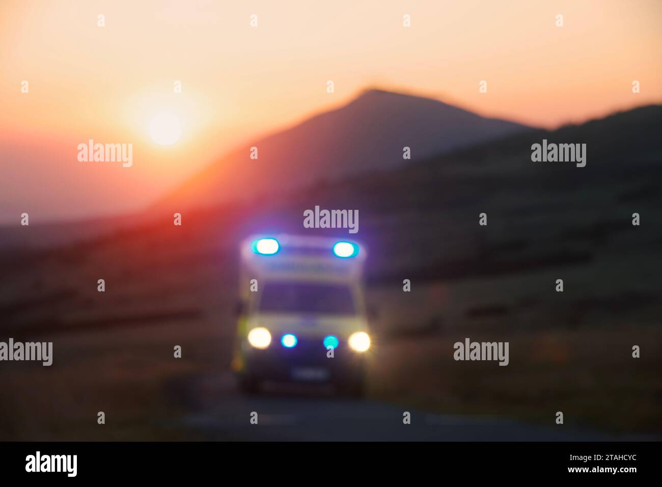Vista sfocata di ambulanza auto di servizio medico di emergenza su strada di montagna all'alba. Temi assistenza sanitaria, soccorso e urgenza. Foto Stock