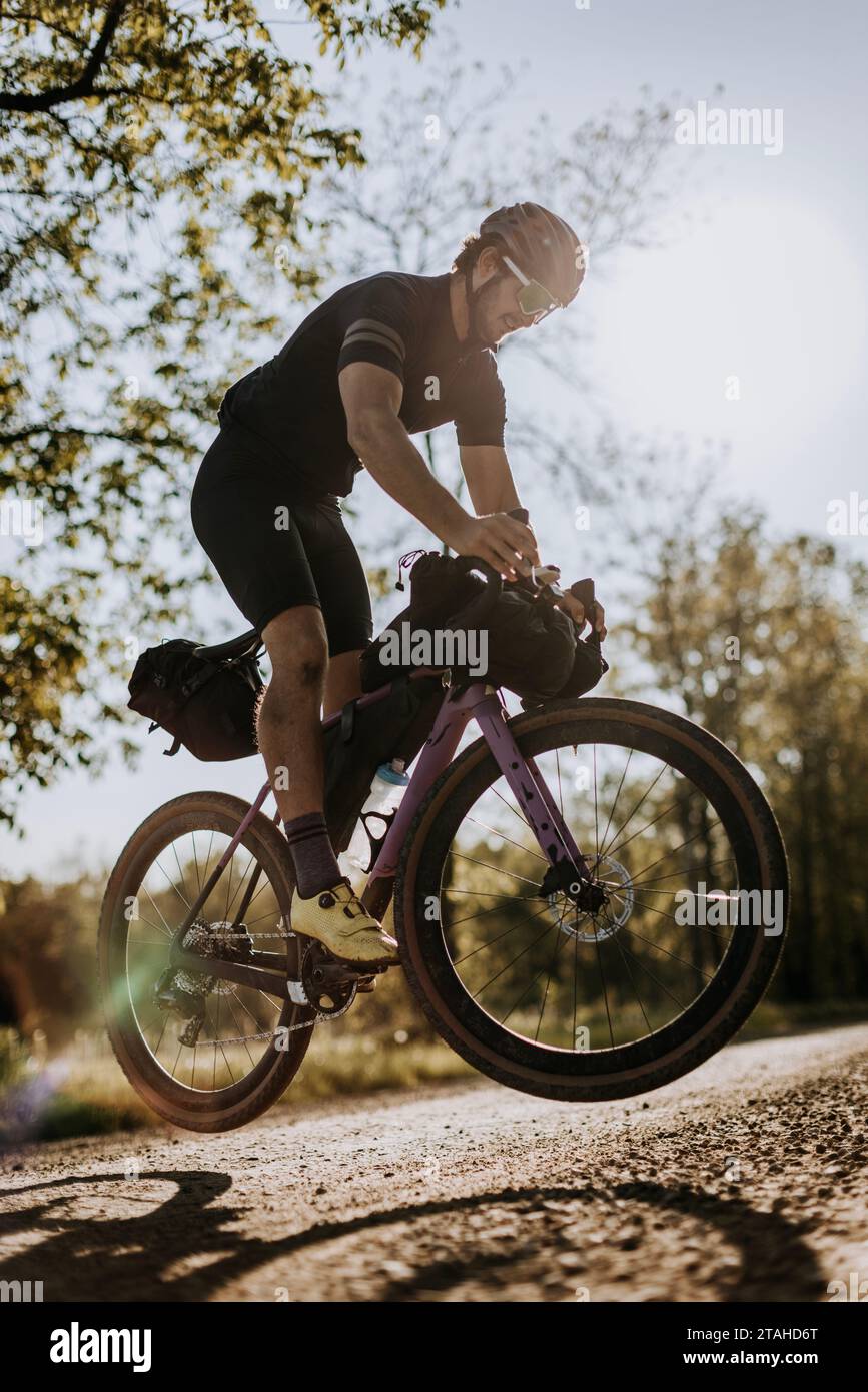 Un ciclista maschile in bicicletta viola fa un bunny hop su una strada ghiaiosa Foto Stock