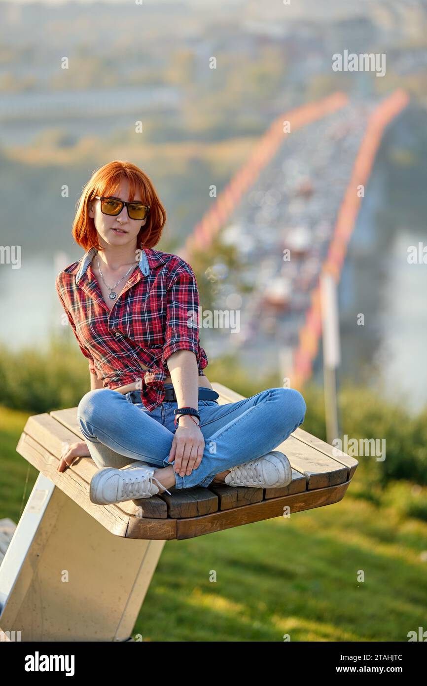 Una donna alla moda rossa che si gode una serata autunnale in città. Indossa una camicia rossa alla moda e jeans denim, per un'audace dichiarazione di stile Foto Stock