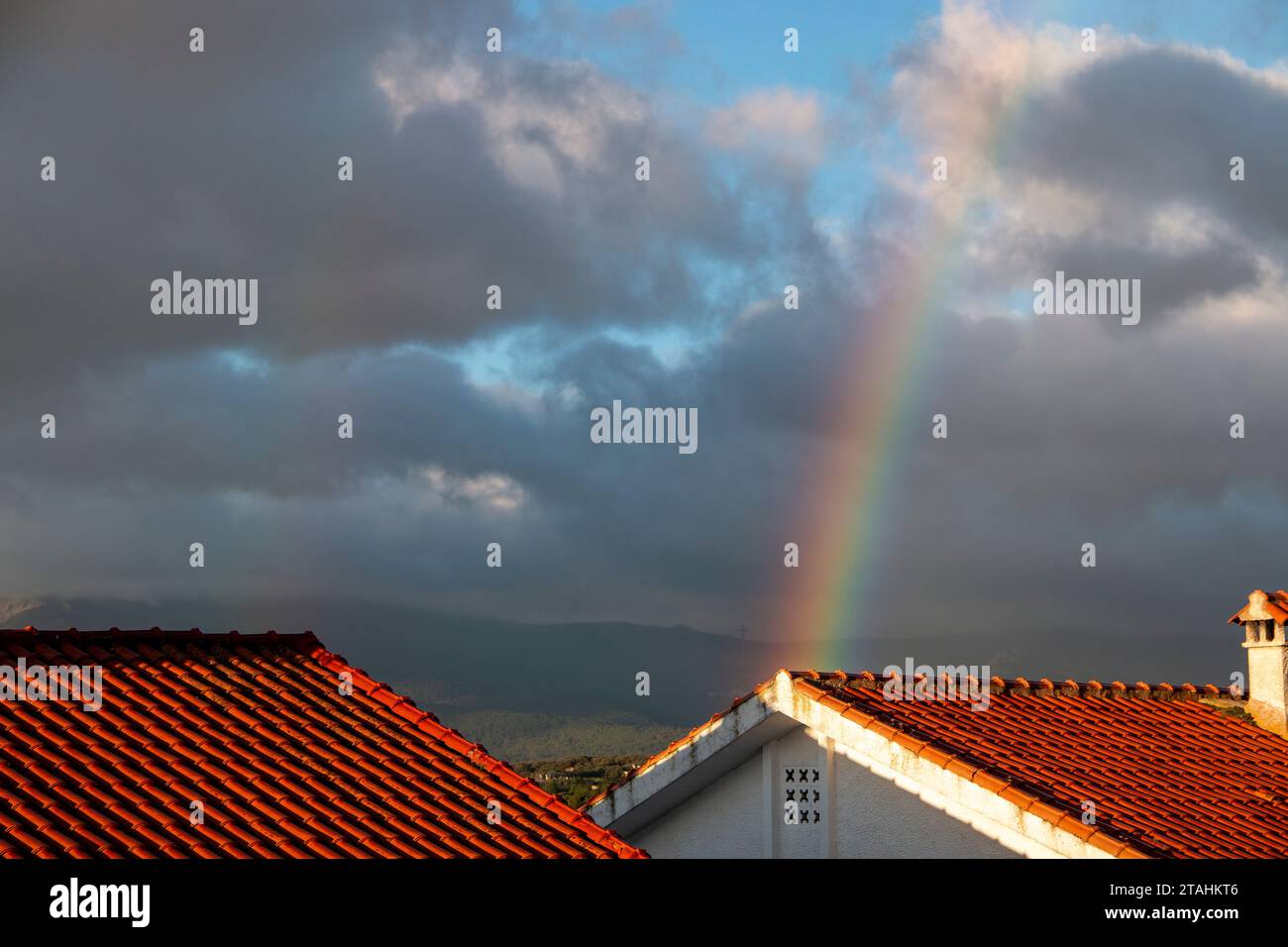 Arcobaleno in una giornata nuvolosa sui tetti delle case Foto Stock