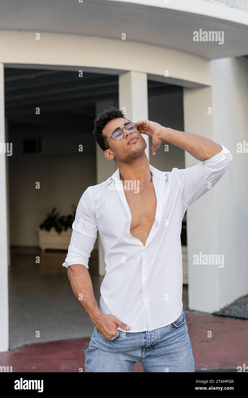 Uomo cubano dall'aspetto rilassato e piacevole con camicia bianca e occhiali rotondi che toccano i capelli ricci Foto Stock