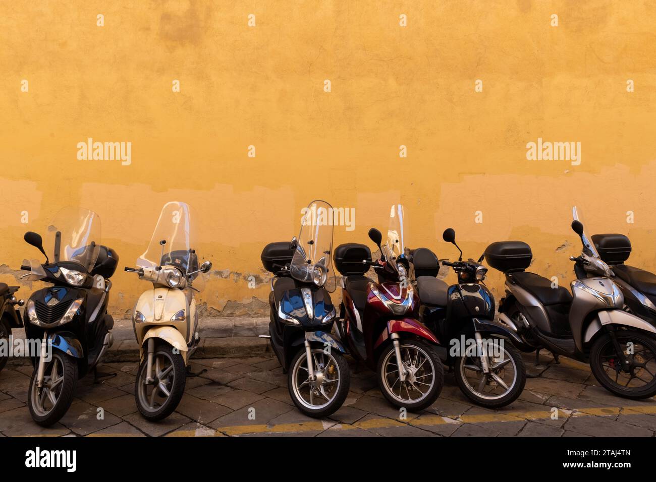 Più scooter parcheggiati di fronte a una parete gialla brillante su un marciapiede a Firenze, Italia. Foto Stock