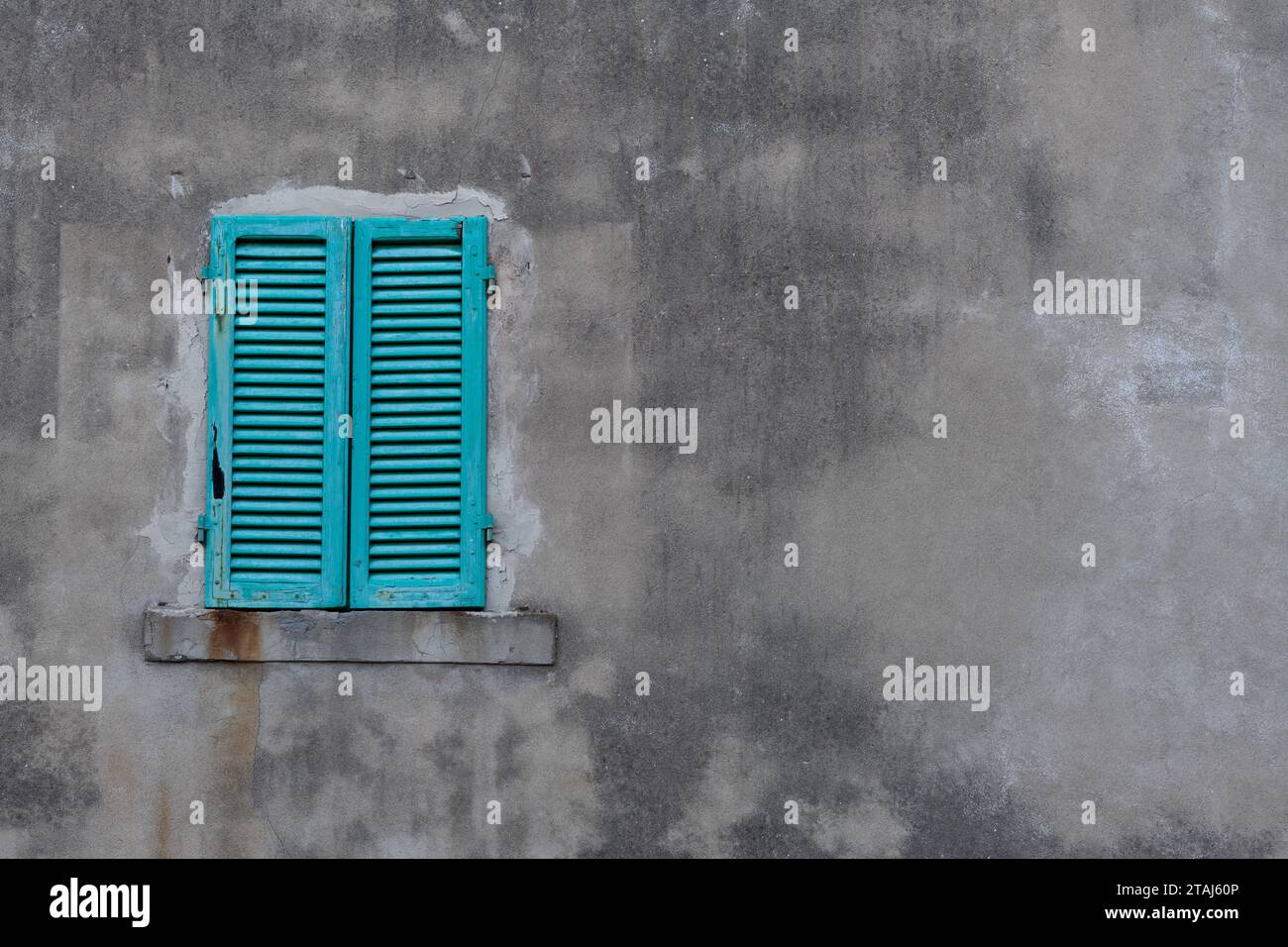 Persiane in legno color turchese, di colore brillante chiuse su un grande muro di cemento grigio su un edificio in Toscana, Italia. Foto Stock