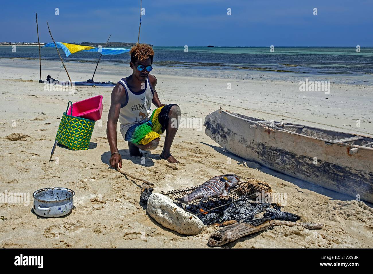 Uomo malgascio che cucina pesce appena pescato alla griglia sul fuoco di carbone sulla spiaggia sabbiosa di Andavadoaka vicino a Morombe, regione di Atsimo-Andrefana, Madagascar Foto Stock