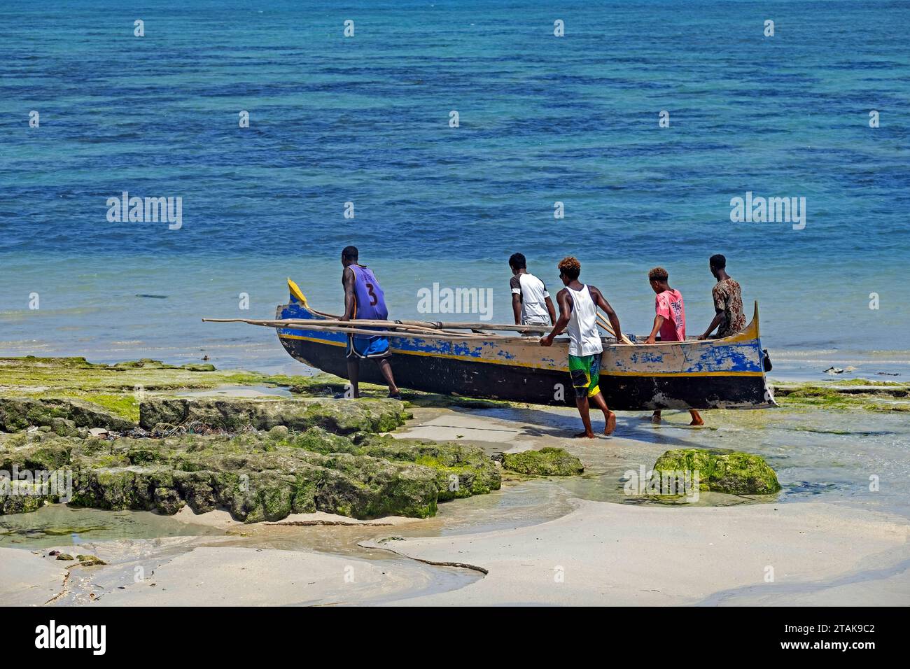 Pescatori malgasci che trasportano barche da pesca in legno sulla spiaggia al mare nel villaggio di pescatori Andavadoaka vicino a Morombe, regione di Atsimo-Andrefana, Madagascar Foto Stock