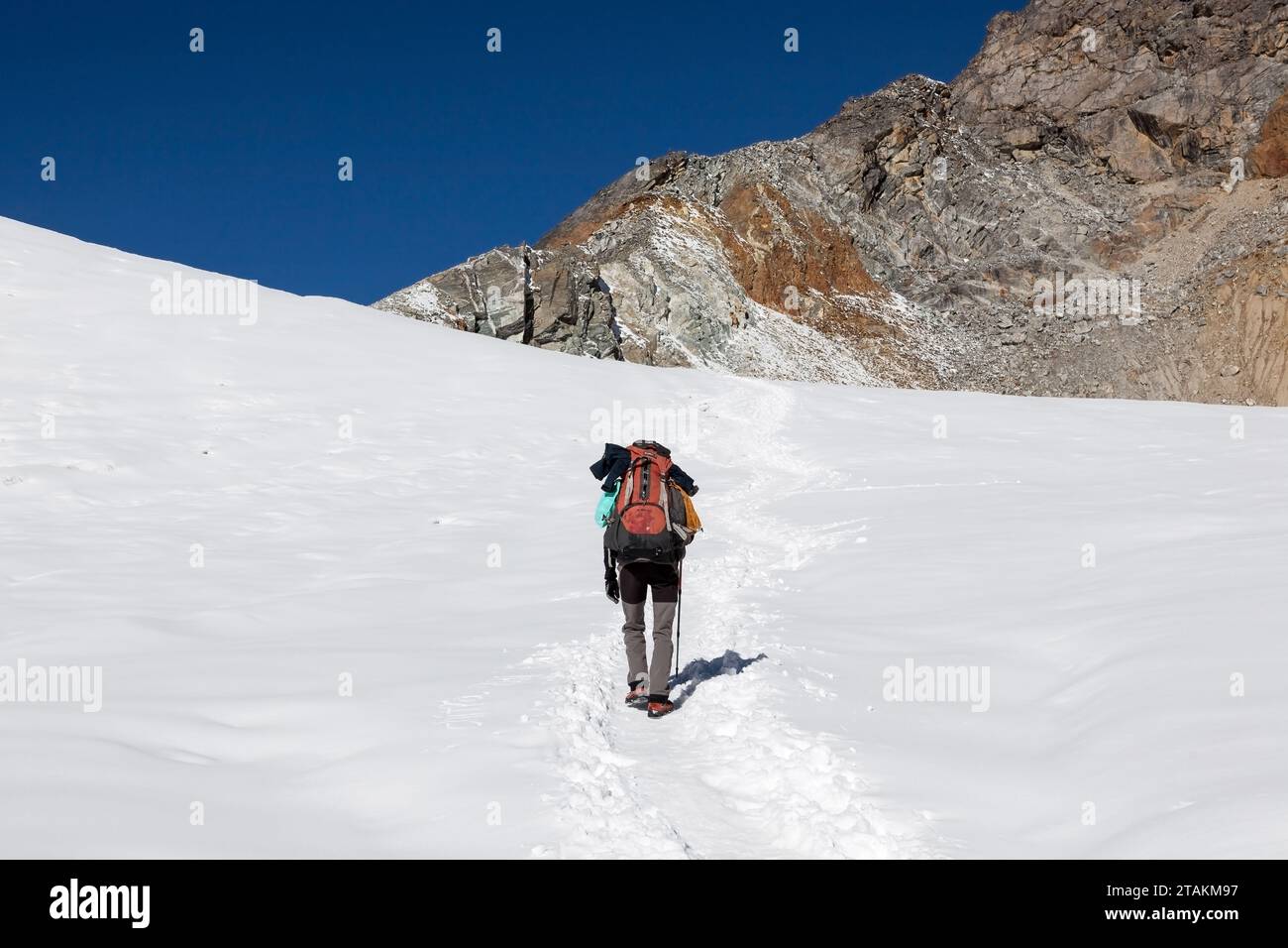 Concetto di escursionismo estremo da solo. Viaggiatore singolo che cammina su per la montagna nella neve profonda con un grande zaino pesante e un'asta da trekking. Foto Stock
