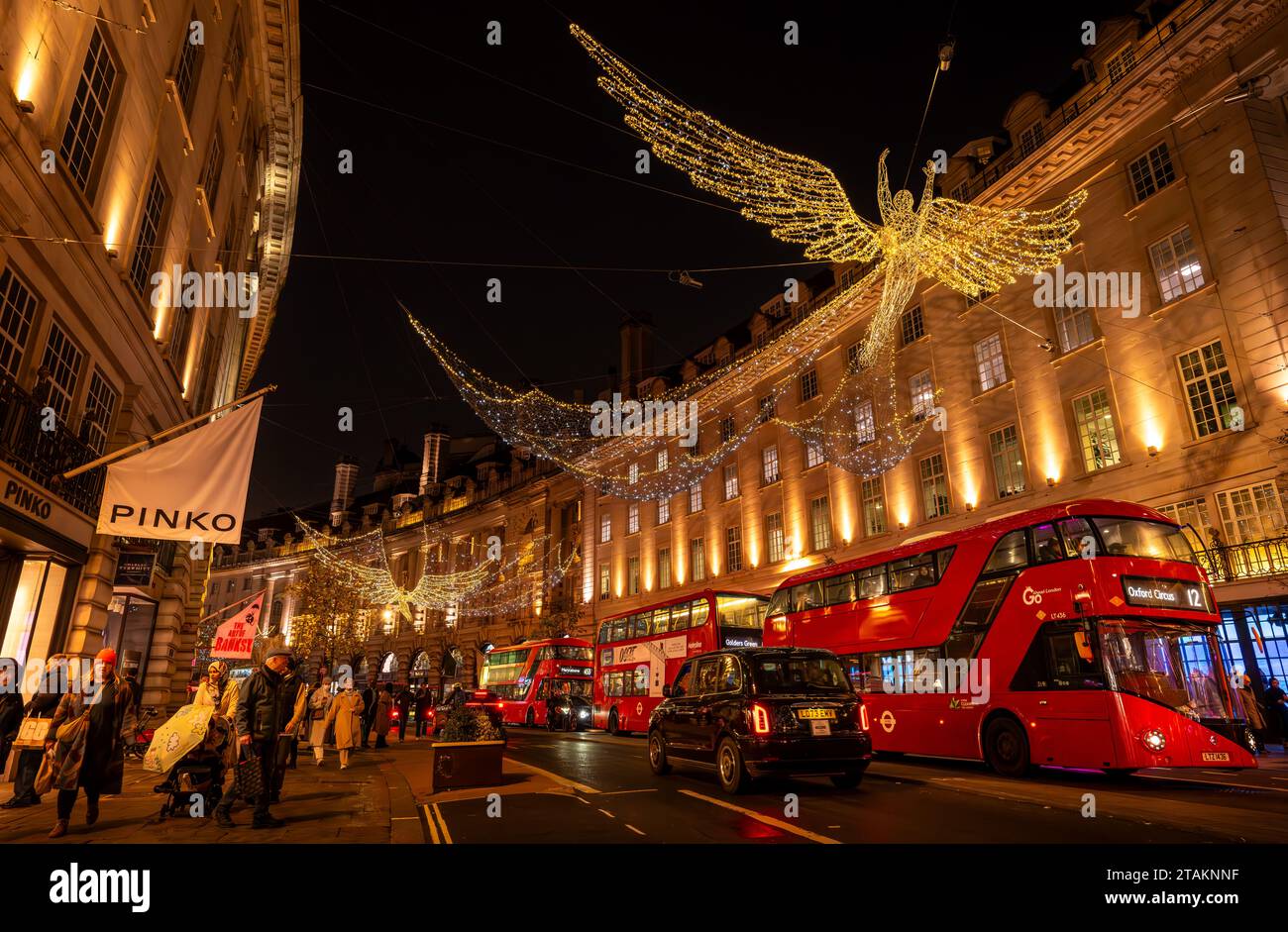 Londra, Regno Unito - 20 novembre 2023: Regent Street con luci natalizie in alto. La gente fa shopping natalizio e si avvicina a tre autobus rossi di Londra. Foto Stock