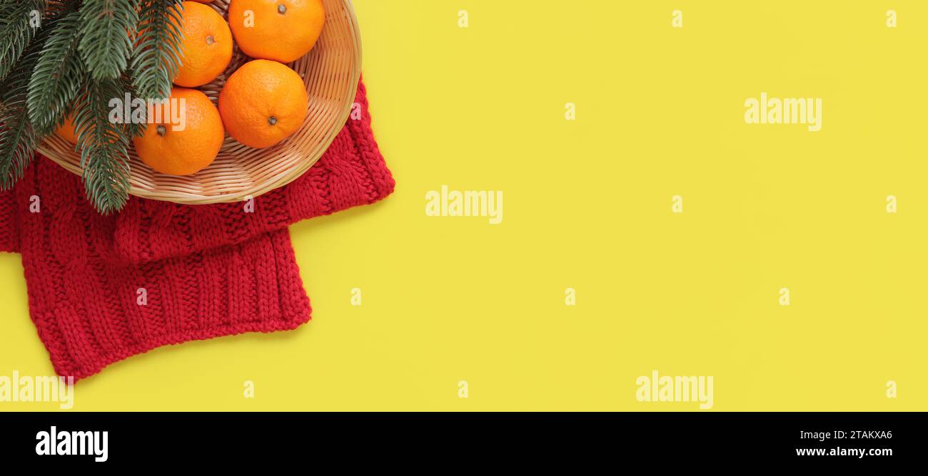Mandarini in un cesto, una sciarpa a maglia rossa e rami di abete su sfondo giallo. Composizione natalizia, anno nuovo, banner. Arredamento di Capodanno. Copia S Foto Stock