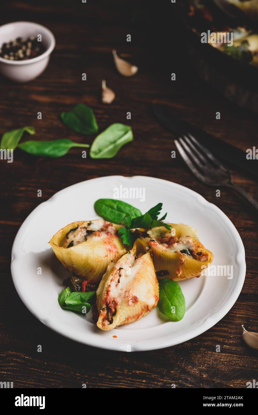 Conchiglie di jumbo al forno farcite con manzo macinato, spinaci e formaggio su piatto bianco Foto Stock
