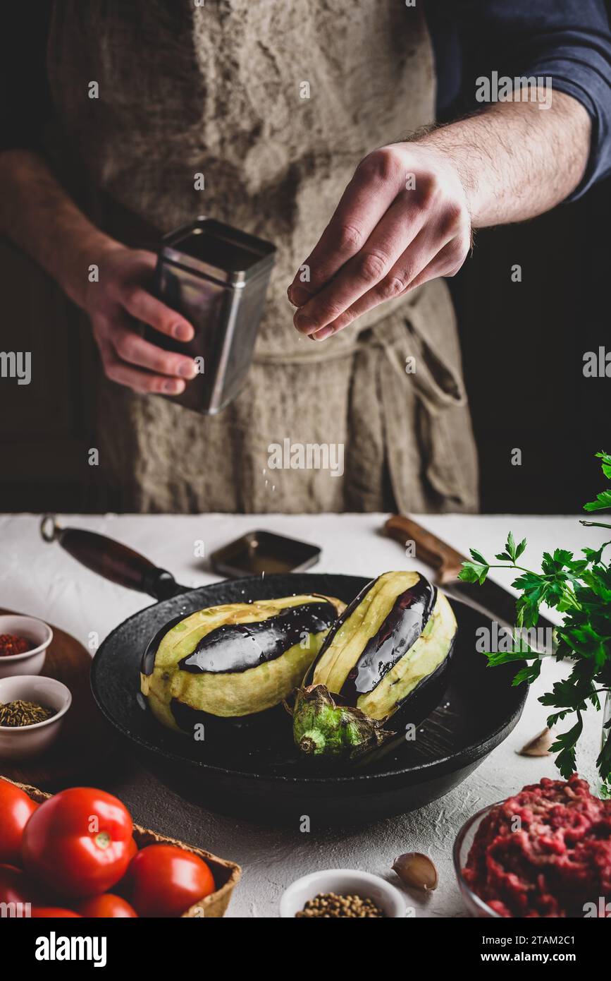 Preparazione delle melanzane per la cottura e ripieno con carne macinata e pomodori. Sale spruzzante Foto Stock