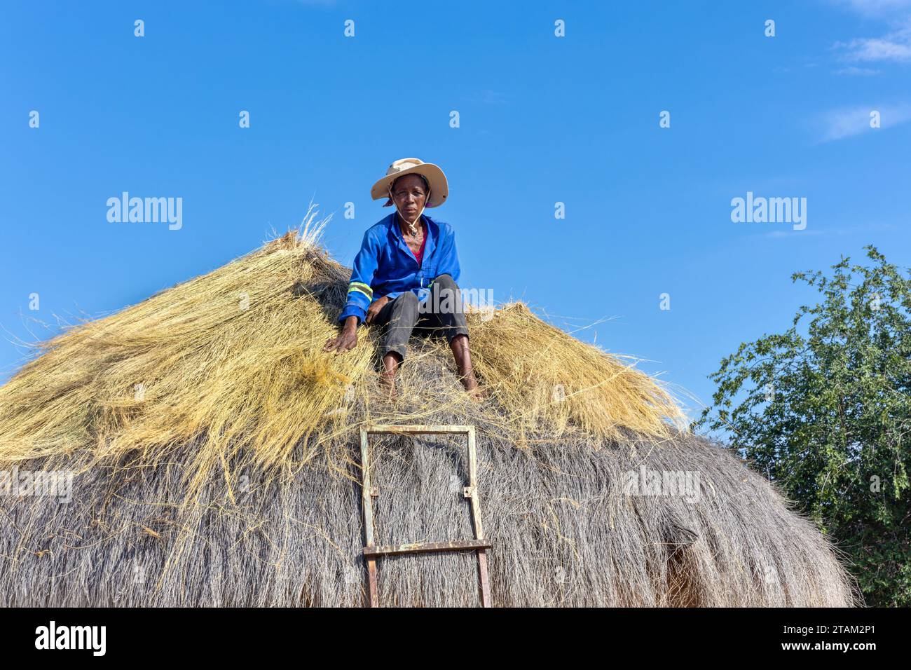 una donna africana si arrampicò per riparare un tetto di paglia su una capanna Foto Stock