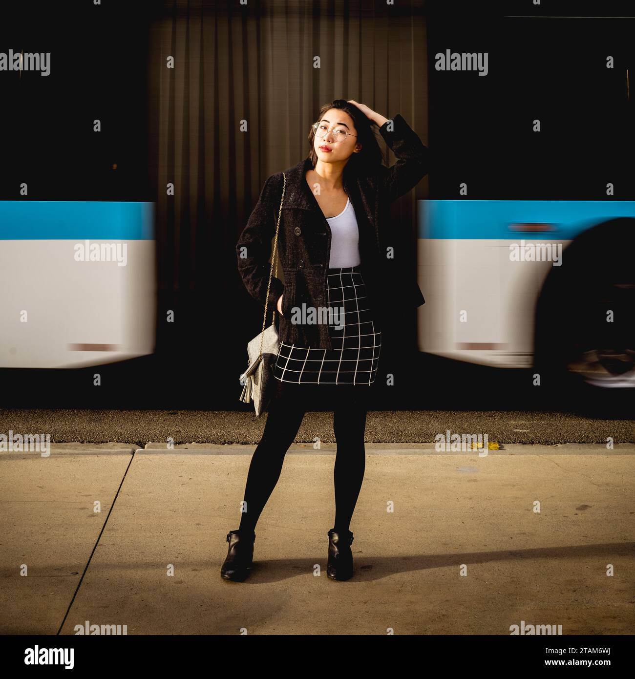 Giovane donna asiatica in piedi abbigliamento da lavoro informale sul marciapiede del centro città in movimento autobus in background Foto Stock