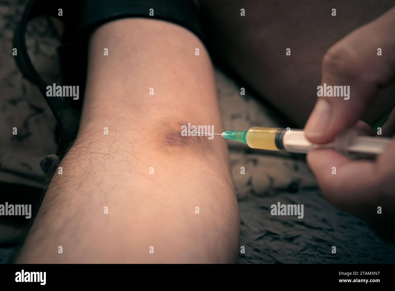Uomo droga addicted l'iniezione di eroina nel suo braccio al tavolo con altri farmaci su sfondo nero nel buio Foto Stock