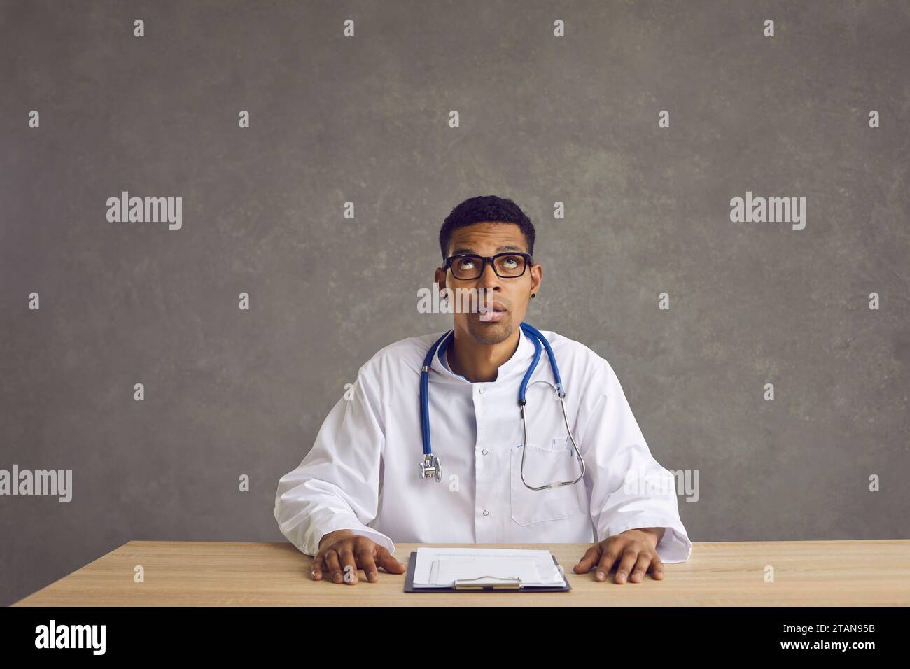 Un giovane medico nero seduto alla scrivania, guarda in alto e pensa a qualcosa Foto Stock