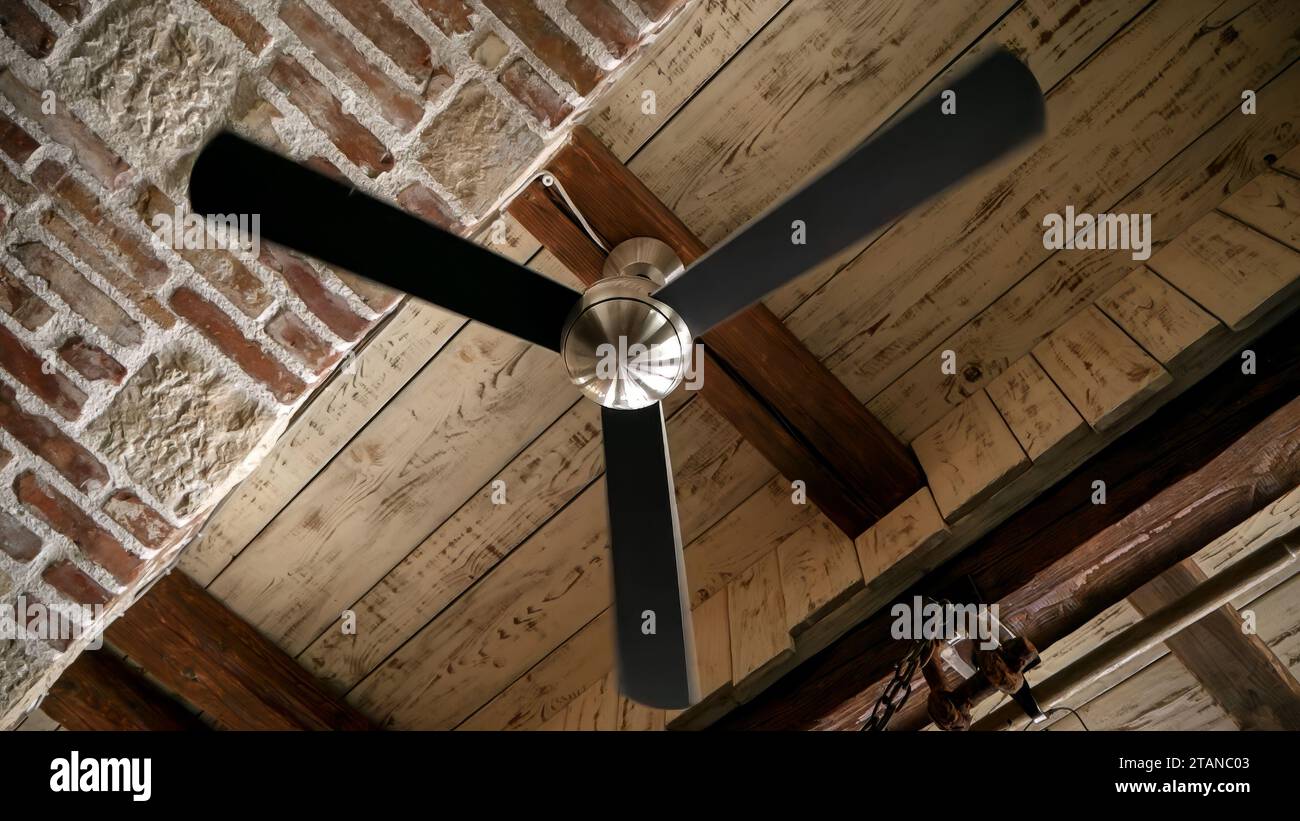 Ventilatore d'aria a soffitto che gira lentamente su vecchi soffitti in legno e mattoni antichi. Foto Stock