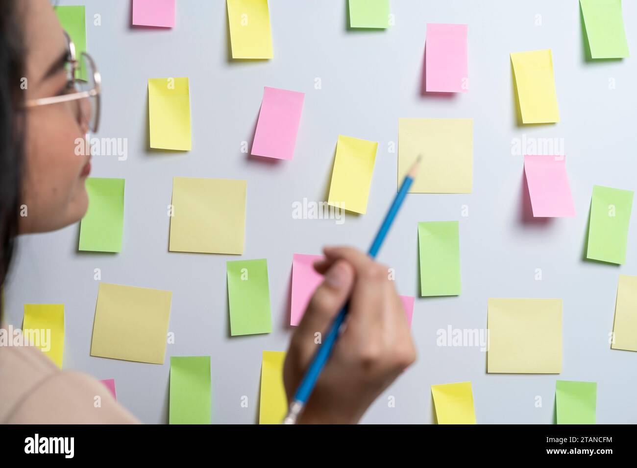 Una giovane donna che scrive promemoria o cose da fare su un biglietto e lo attacca al muro Foto Stock