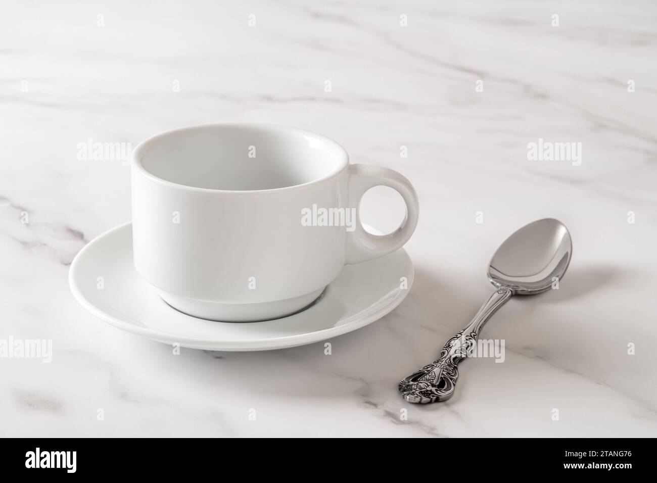 Tazza bianca sul piattino e cucchiaino sul tavolo di marmo. Svuotare le stoviglie in porcellana pulite per un mockup di design delle bevande. Stoviglie, colazione, tè e caffè. Foto Stock