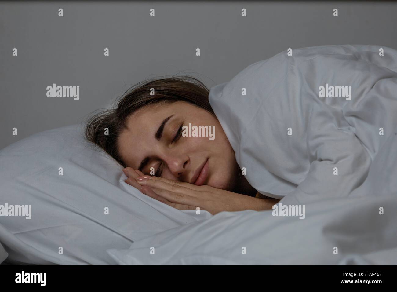 La ragazza sta dormendo in un letto con un lenzuolo bianco. Foto Stock