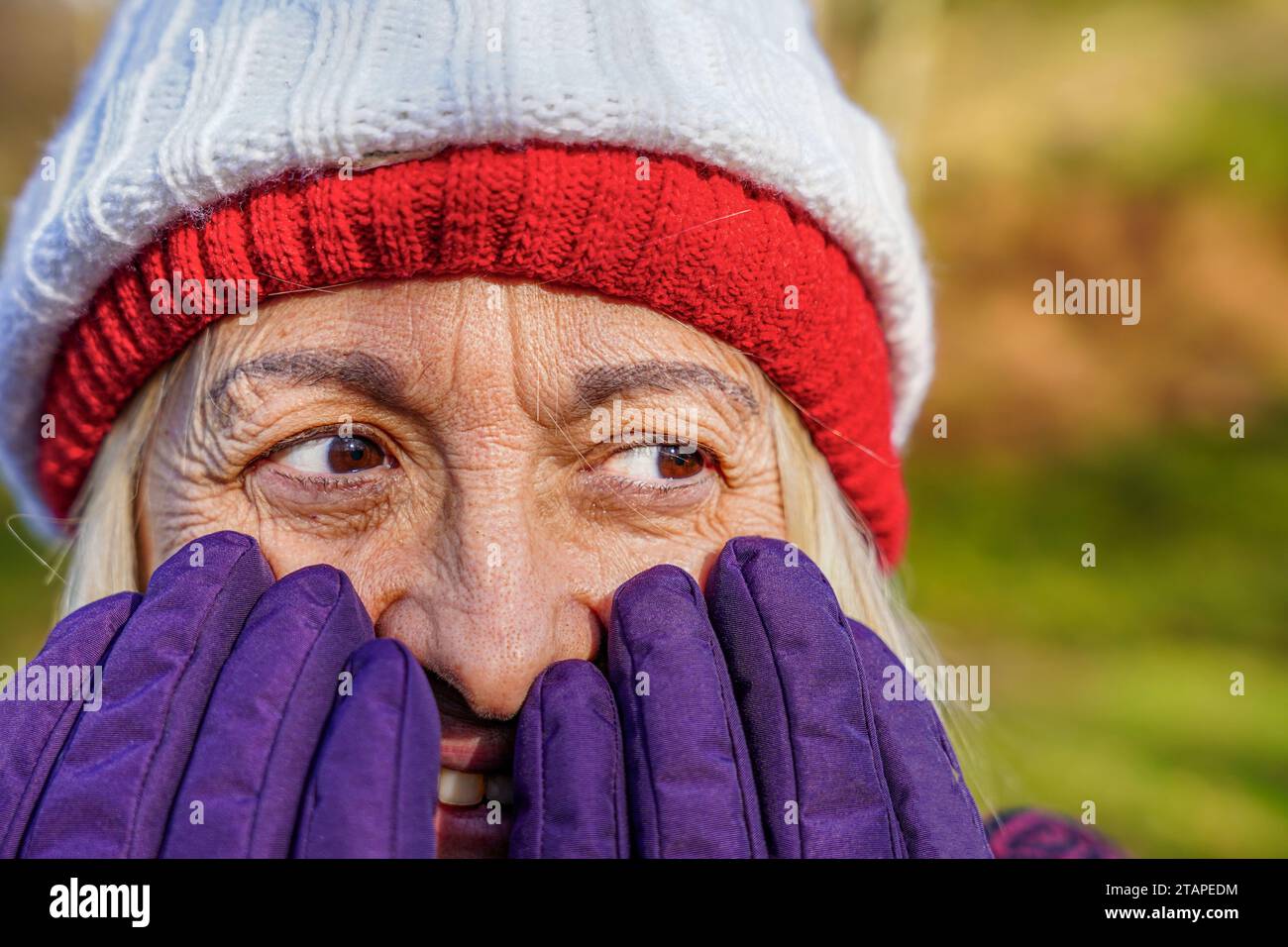 Volto di donna matura nascosto dietro i guanti invernali con cappello a maglia Foto Stock