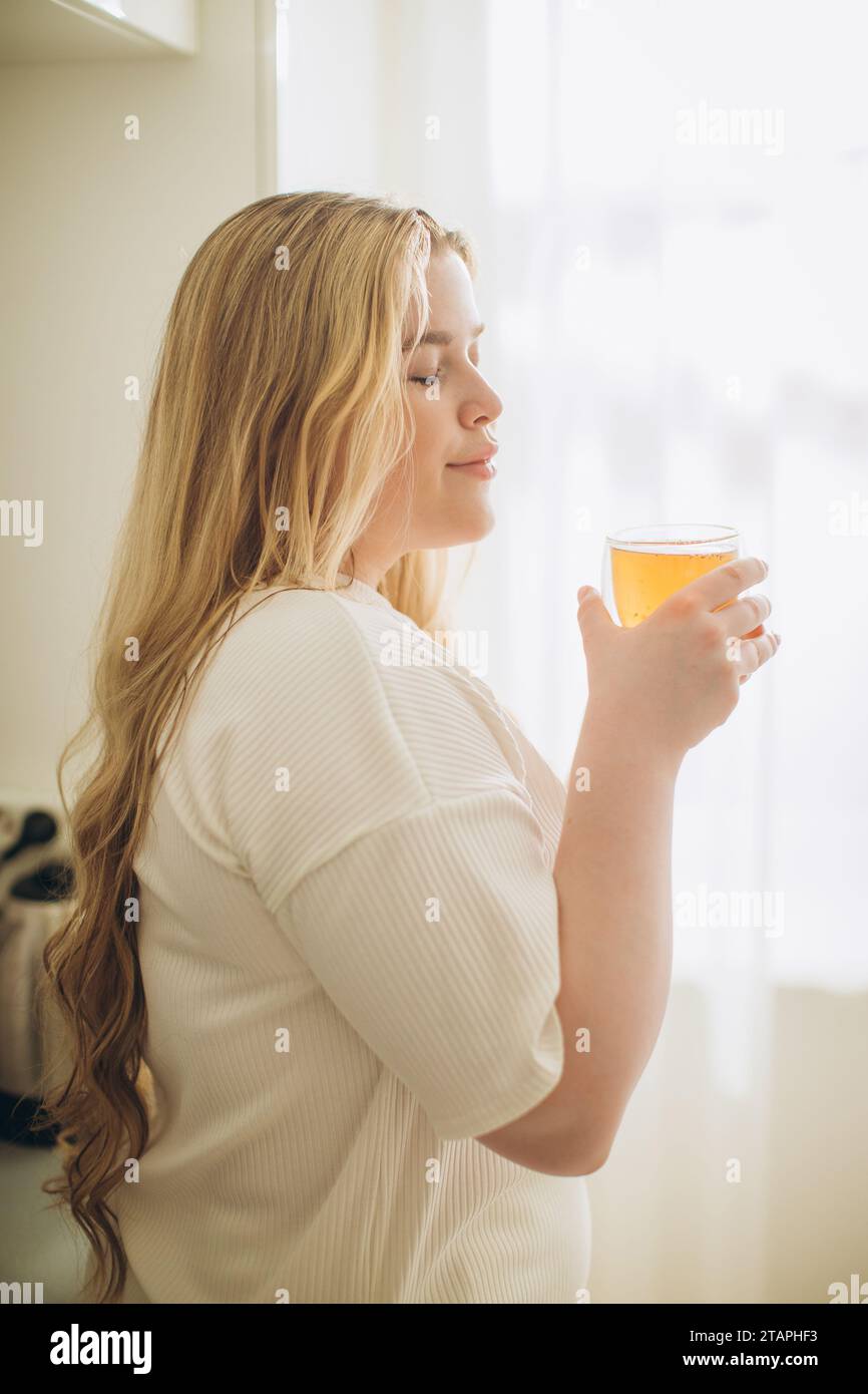 Ritratto di una giovane donna sorridente che tiene in mano una tazza di tè caldo al mattino in una cucina Foto Stock