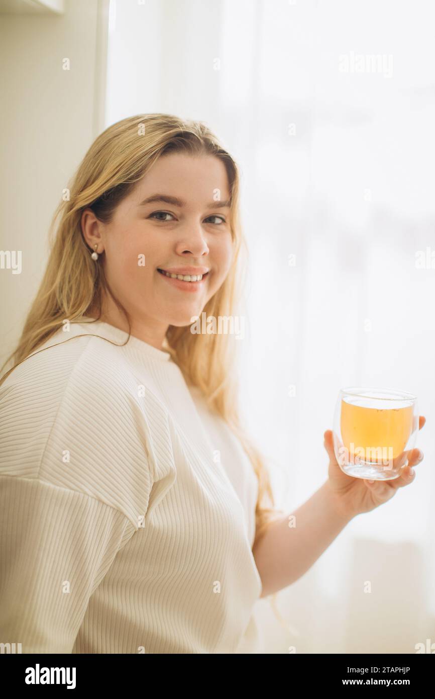 Ritratto di una giovane donna sorridente che tiene in mano una tazza di tè caldo al mattino in una cucina Foto Stock