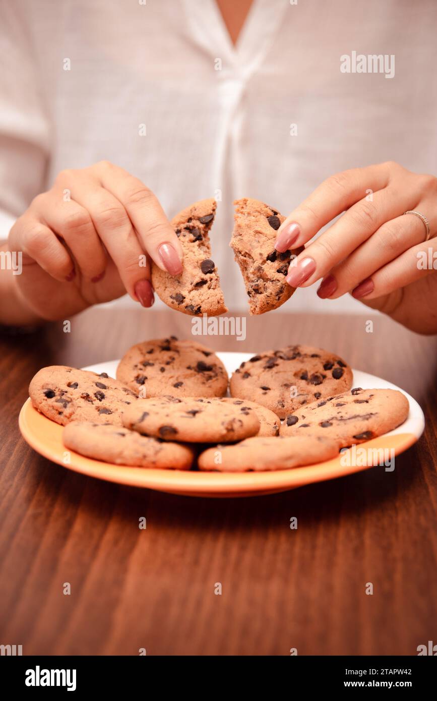 la donna rompe a metà biscotti croccanti con gocce di cioccolato. la donna mangia biscotti Foto Stock