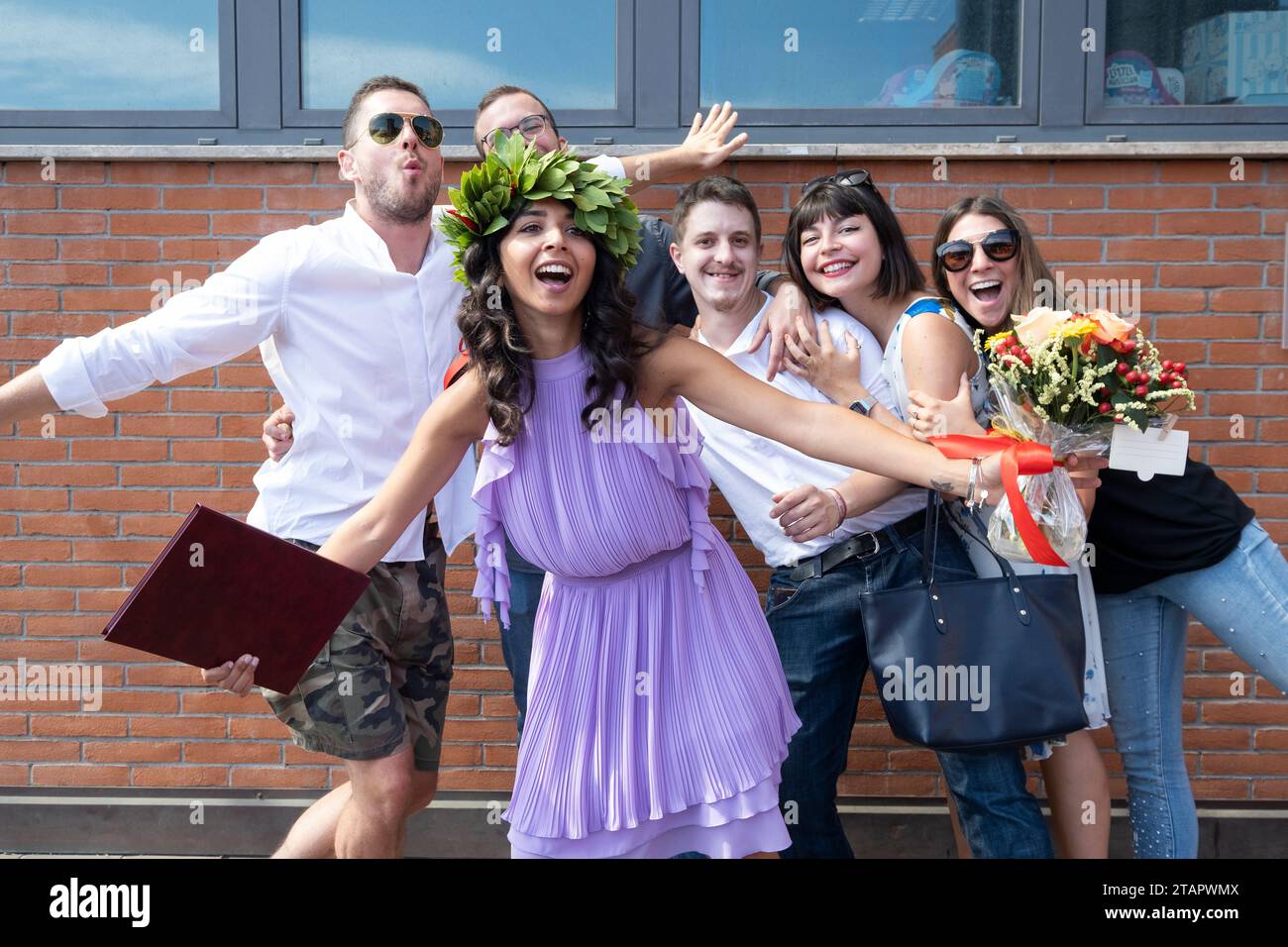 Gruppo di giovani allegri che si posa davanti alla telecamera con una ragazza laureata che indossa la corona delle foglie. Italia Foto Stock
