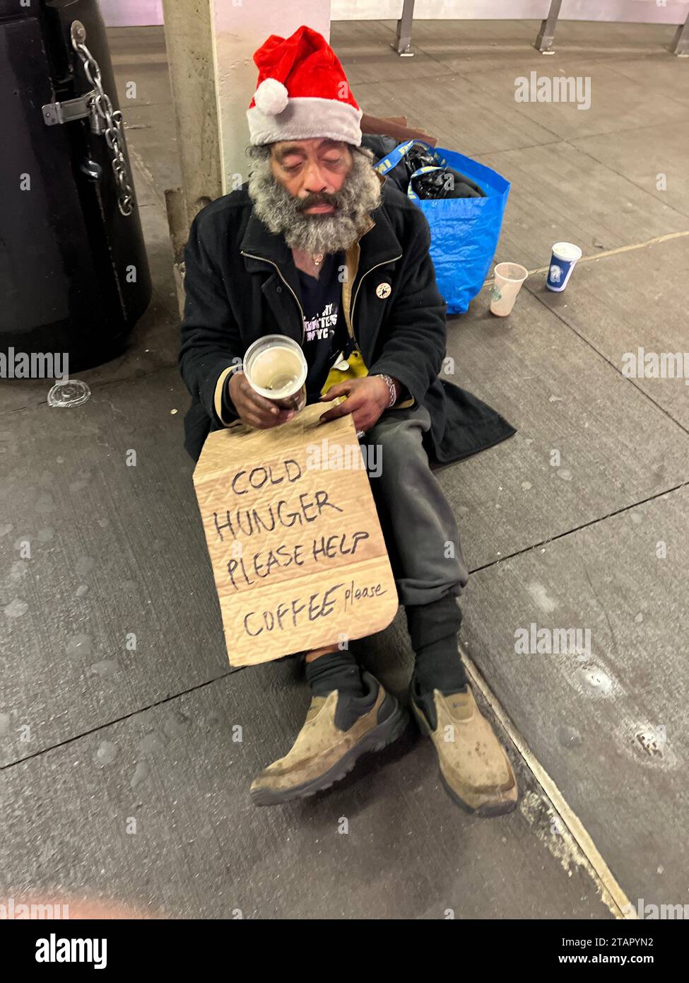 Un senzatetto con un cappello di Babbo Natale chiede aiuto alla stazione della metropolitana di Bleeker Street all'inizio della stagione delle vacanze a Manhattan, New York. Foto Stock