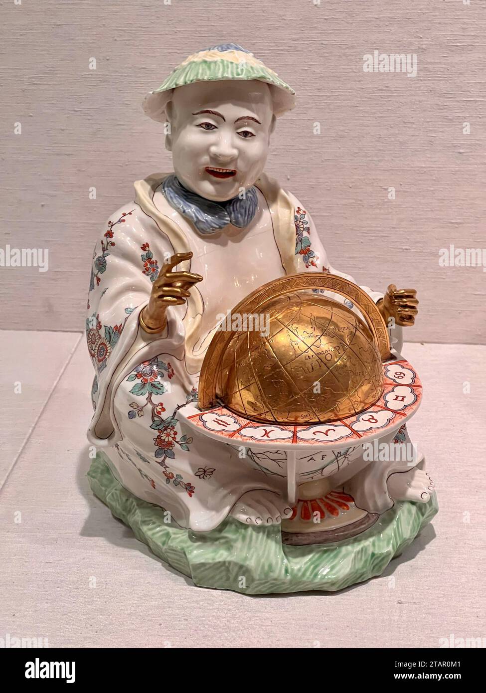 Figura seduta con globo, Francia, ca. 1735. MET Museum, New York. Nel XVII e XVIII secolo, i paesi asiatici furono una fonte di notevole fascino e fascino per gli europei. Le figure asiatiche venivano spesso scelte come soggetti per decorare le ceramiche e altre opere d'arte prodotte in Europa, ma queste raffigurazioni erano raramente basate su conoscenze di prima mano e quindi erano di solito fantasiose. Questa figura di un uomo cinese seduto con un globo doveva essere decorativa, ma potrebbe anche alludere alla sofisticata comprensione dell'astronomia cinese durante questo periodo. Foto Stock