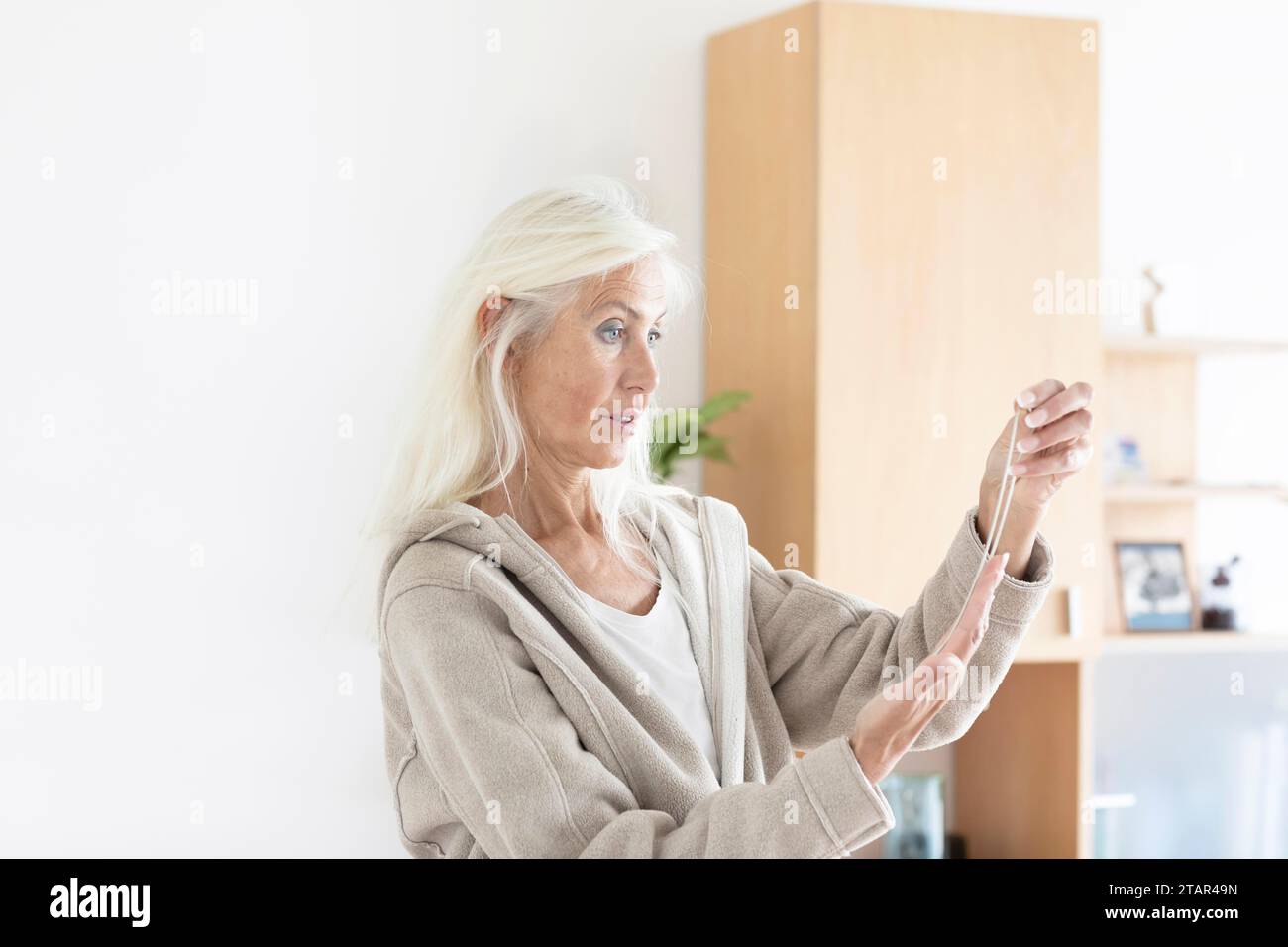 Donna anziana con capelli lunghi che guarda una collana a casa Foto Stock