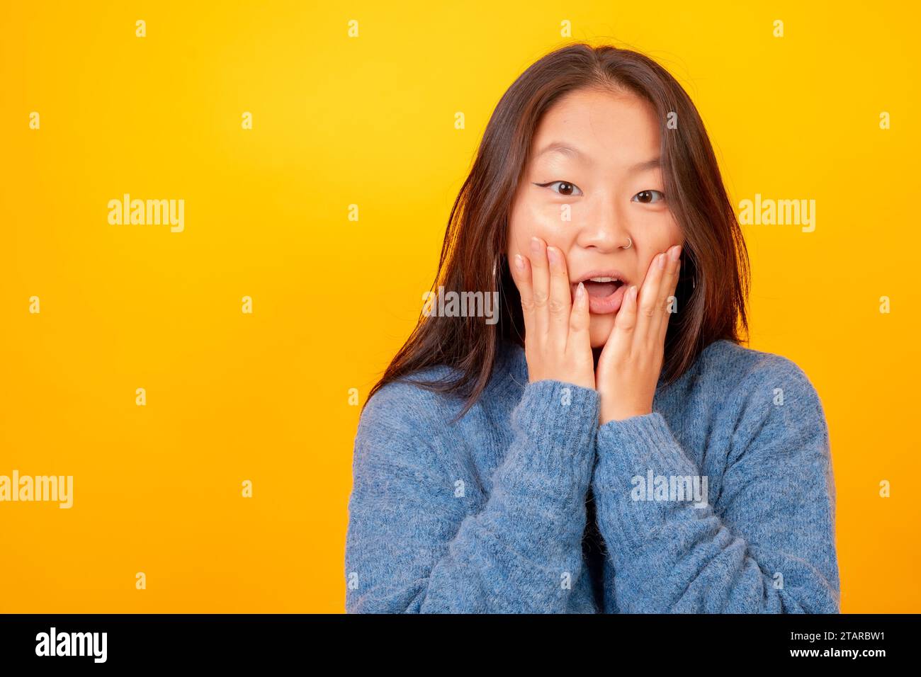 Foto in studio con sfondo giallo di una donna cinese sorpresa con la mano sul viso Foto Stock