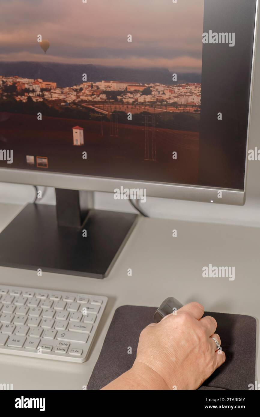 La mano di una donna che lavora al suo computer con un mouse ergonomico verticale per evitare dolori alle mani Foto Stock