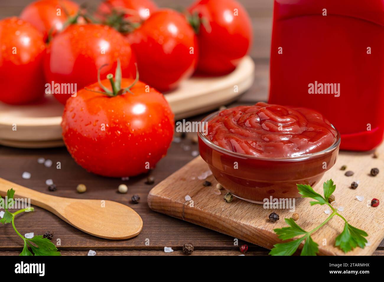 Ciotola di vetro di ketchup o salsa di pomodoro, spezie e pomodori freschi su tavola di legno. Messa a fuoco selettiva. Foto Stock