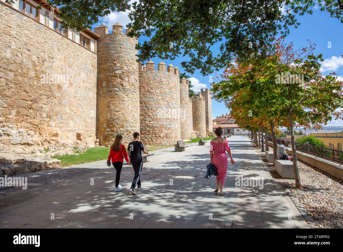 Gente che cammina accanto ai bastioni delle mura fortificate della città fortificata spagnola di Avila, nella comunità autonoma di Castiglia e León Spagna Foto Stock