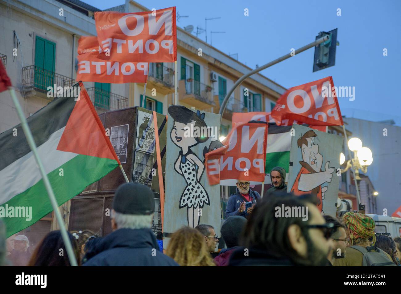 Messina, Italia. 2 dicembre 2023. Wilma e Fred Flintstones circondati da bandiere "senza ponte" (coloro che non vogliono il ponte sono stati definiti "cavernicoli") durante la protesta contro la costruzione del ponte sullo stretto organizzata dal coordinamento senza ponte a Messina. Circa duemila persone hanno protestato contro la costruzione del Ponte sullo stretto di Messina, il ponte sospeso più lungo del mondo in un'area soggetta a venti violenti, forti correnti di marea in una delle zone a più alto rischio sismico del Mediterraneo. Centinaia di migliaia di metri quadrati Foto Stock