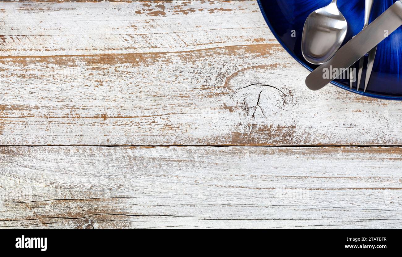 Tavolo da pranzo parziale con posate e piatti blu scuro su un tavolo rustico di legno bianco con vista dall'alto o da terra Foto Stock