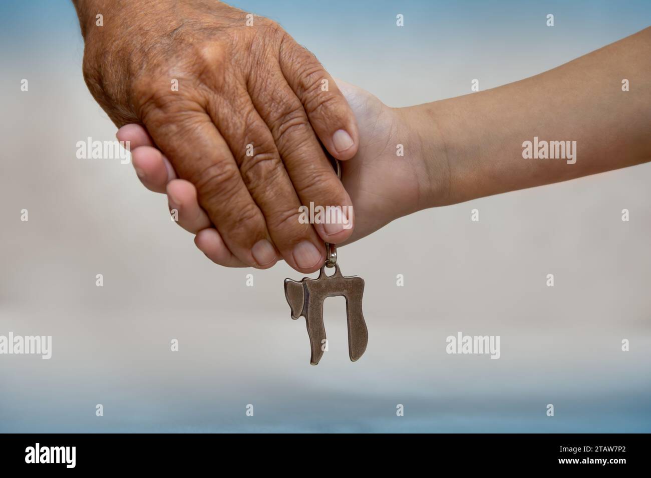 AM Israel Chai. Mani di un uomo anziano che tiene la mano di un bambino da vicino. Hanno in mano un portachiavi Chai argento, che in ebraico si scrive "vita". blu Foto Stock