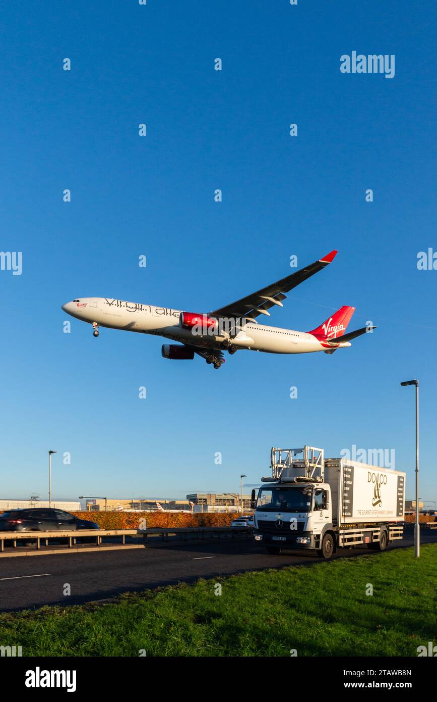 Aeroplano di linea nelle finali per atterrare all'aeroporto di Londra Heathrow, nel Regno Unito, volando sul traffico stradale sulla A30. Virgin Atlantic A330 su furgone catering Foto Stock