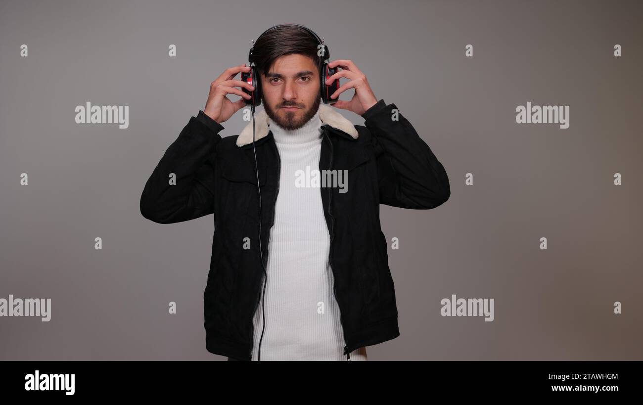 Un giovane su uno sfondo grigio ascolta la musica con le cuffie. Foto Stock