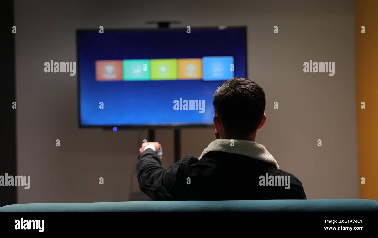 Un giovane che guarda la TV e cambia canale con un telecomando. Foto Stock