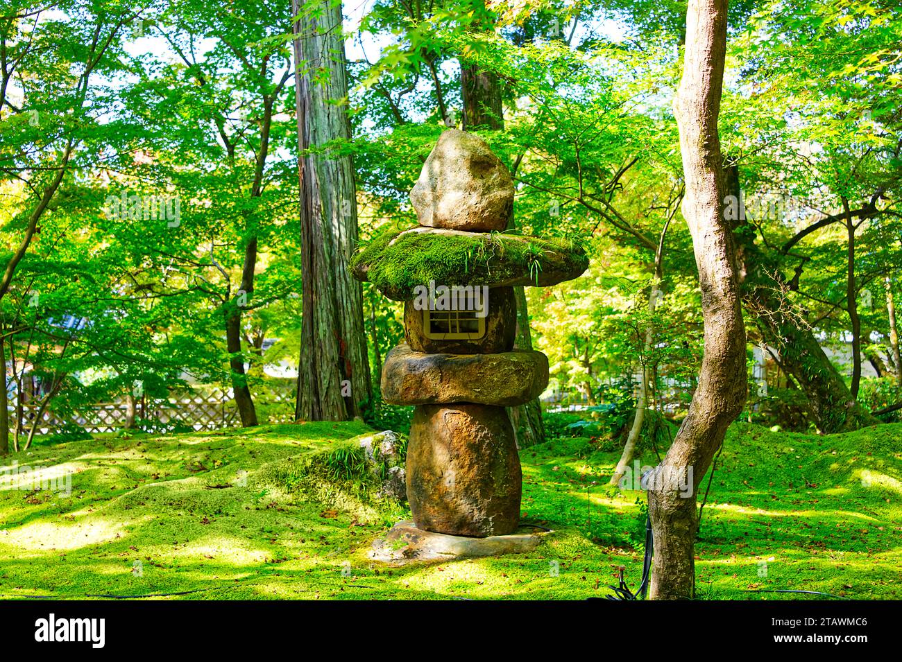 Lanterna giapponese in pietra in un verde parco paesaggistico con alberi ed erba Foto Stock