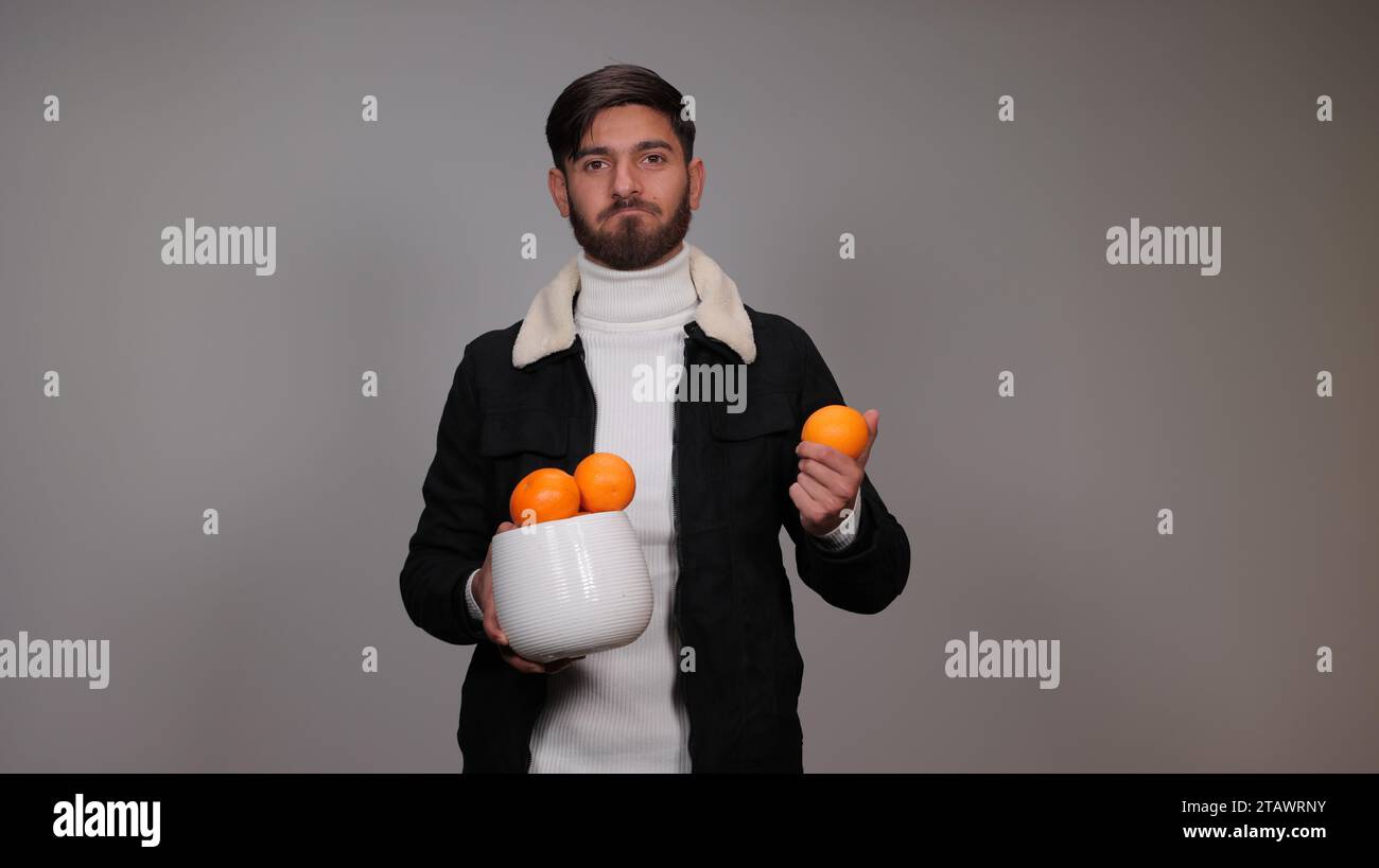 Un giovane che regge un'arancia su sfondo grigio | benefici dell'arancio Foto Stock