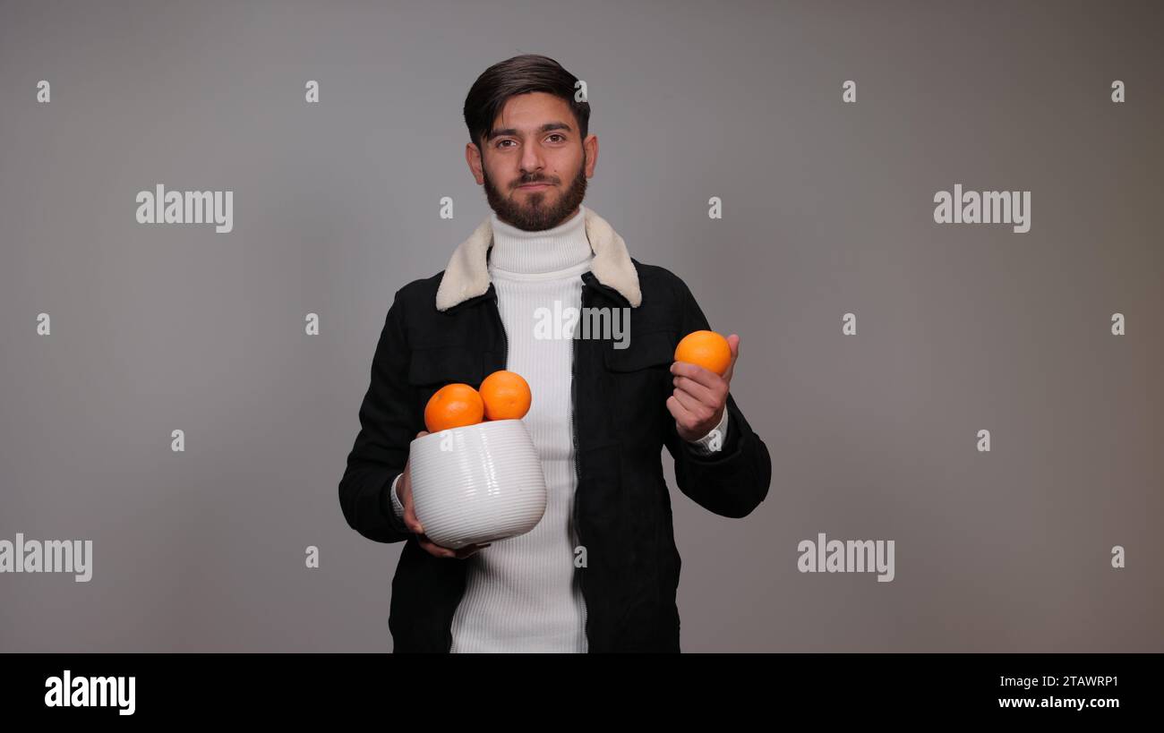 Un giovane che regge un'arancia su sfondo grigio | benefici dell'arancio Foto Stock