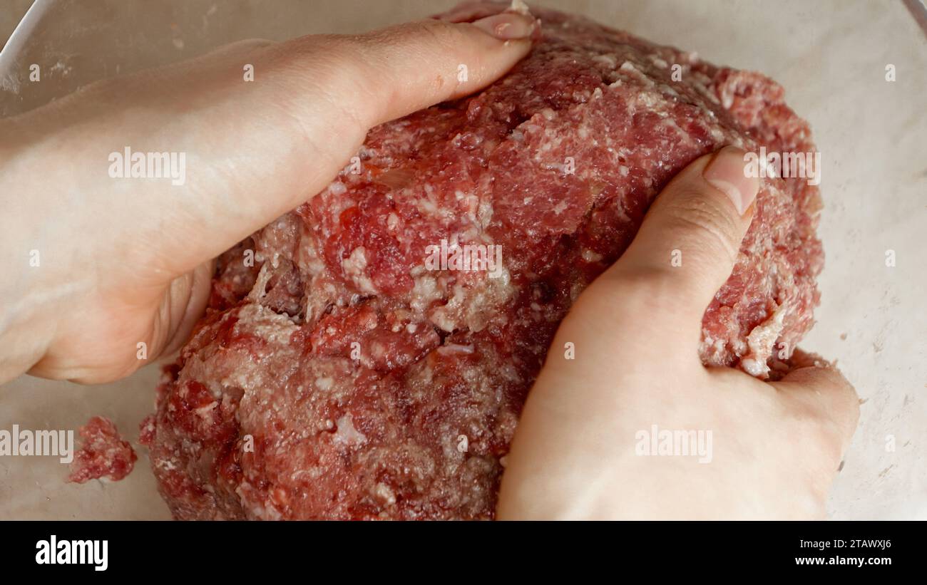 Primo piano delle mani femminili per mescolare e sbattere la carne di manzo macinata prima di preparare gli hamburger. Cucinare a casa Foto Stock